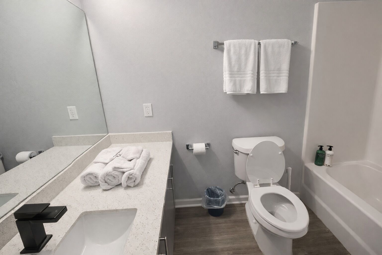 Ein modernes Badezimmer mit Toilette, Waschbecken und Badewanne. Auf der Ablage liegen Handtücher und ein Mülleimer steht bereit.