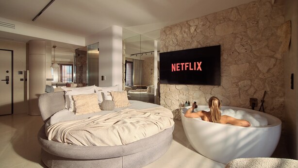 A modern bedroom with a large bed, a bathtub, and a TV displaying 'NETFLIX'. - Granaria Jacuzzi Premium Suites by Downtown Apartments (Gdańsk)