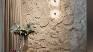 A spa area with a stone wall, a massage table, a small table with a vase of flowers, and two bottles on a small round table. - Granaria Jacuzzi Premium Suites by Downtown Apartments (Gdańsk)