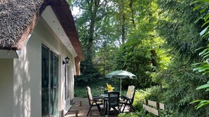 A patio with a table and chairs, a thatched roof, and a wooden fence.