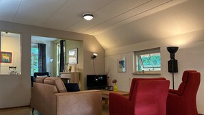 A modern living room with a beige sofa, red armchairs, a flat-screen TV, and a ceiling light.
