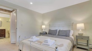 Une chambre à coucher comprenant un lit, deux tables de chevet, une commode, une porte et un luminaire fixé au mur.