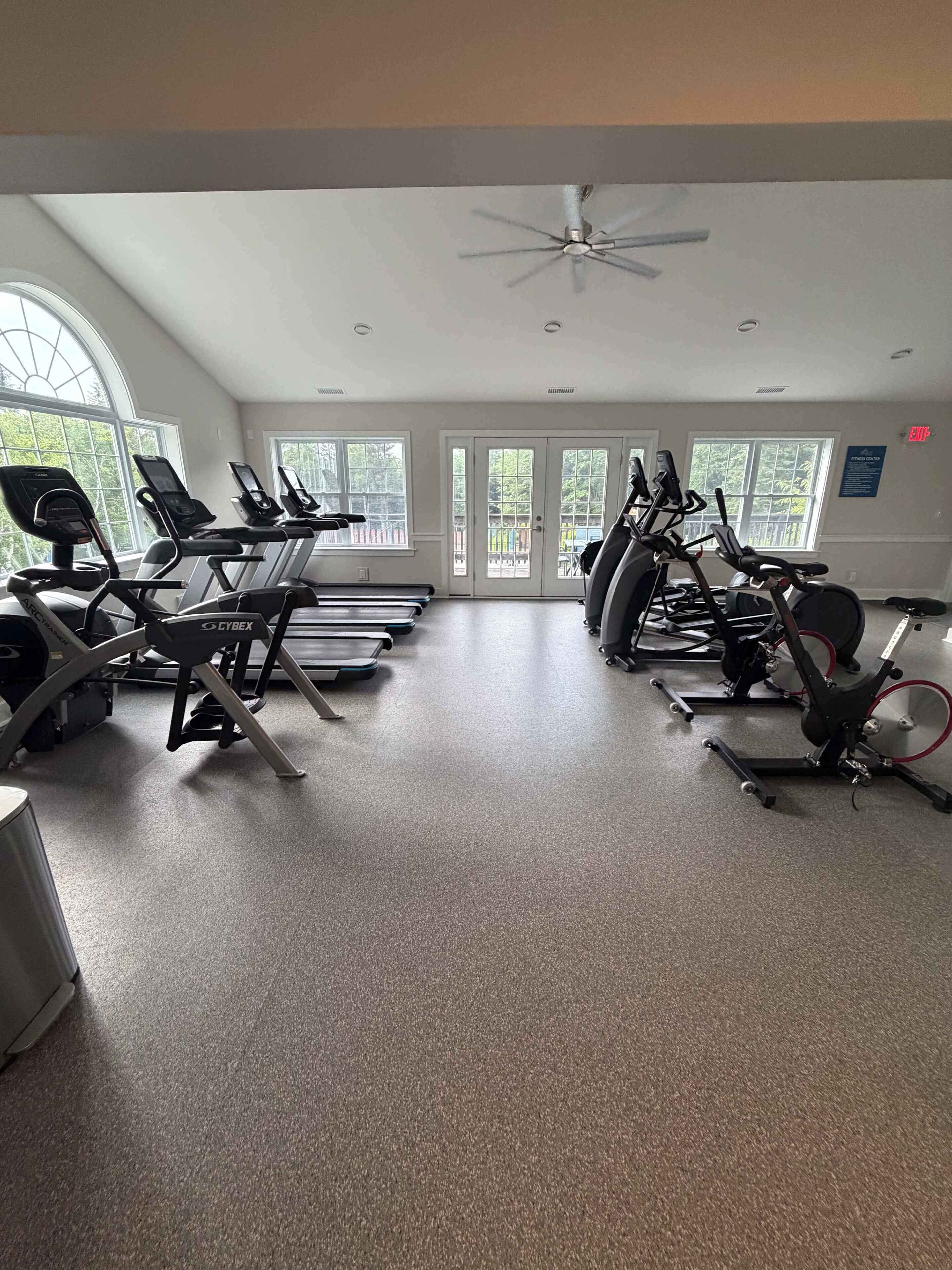 A gym with treadmills, stationary bikes, and a ceiling fan.