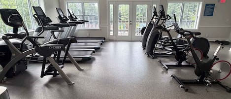 Un gimnasio con cintas de correr, bicicletas estáticas y un ventilador de techo.
