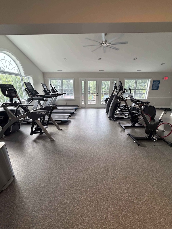 A gym with treadmills, stationary bikes, and a ceiling fan.