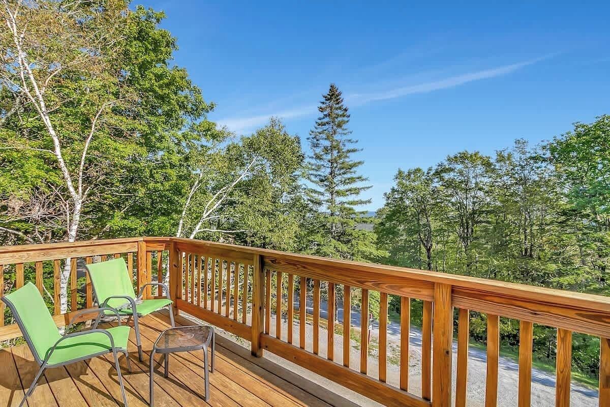 A wooden deck with green chairs and a table, surrounded by trees.