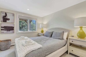 Een slaapkamer met een bed, nachtkastjes, een raam en kunst aan de muur.