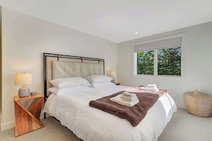 Une chambre à coucher avec un lit, des tables de chevet, une fenêtre et une vue sur la verdure.