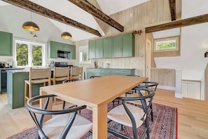 Une cuisine spacieuse avec une table et des chaises en bois, des meubles de couleur verte et une grande fenêtre.