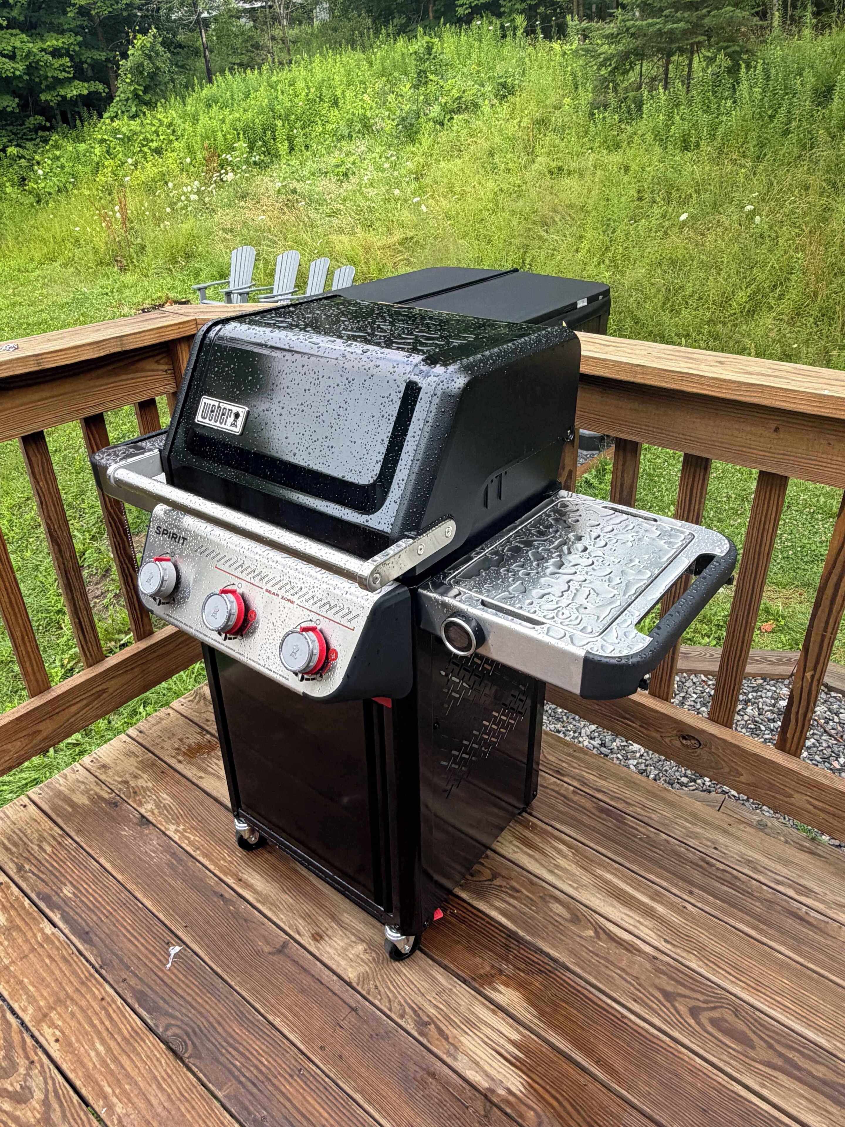 A portable grill on a wooden deck with a grassy background.