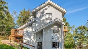 Une maison à deux étages dotée d’une terrasse en bois et d’un petit escalier menant à l’entrée.