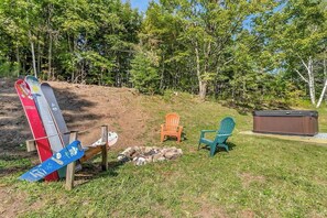 Un espace extérieur verdoyant avec un foyer, des fauteuils Adirondack et un jacuzzi.