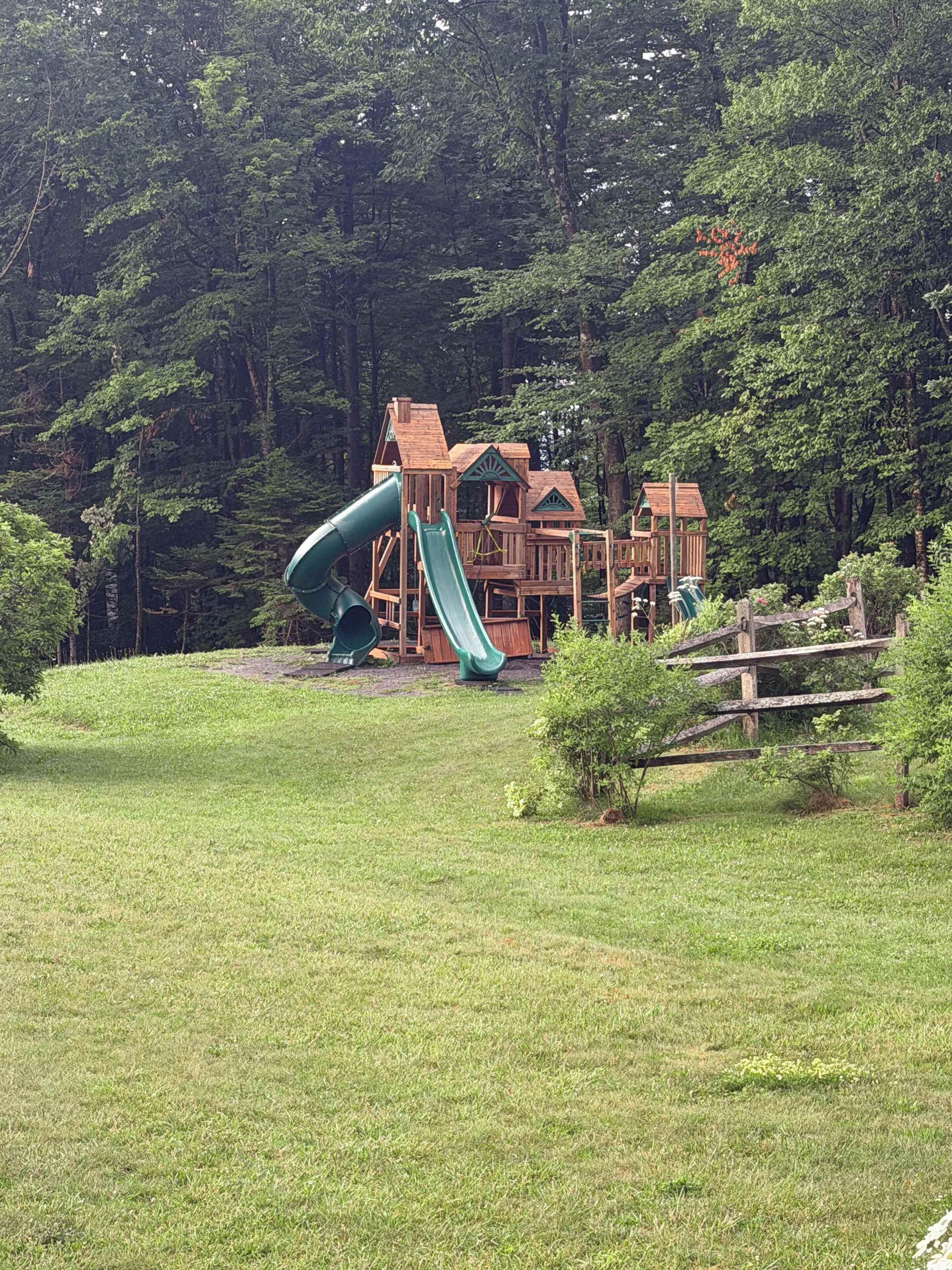 Un parque infantil con tobogán y estructuras para escalar, rodeado de césped y árboles.