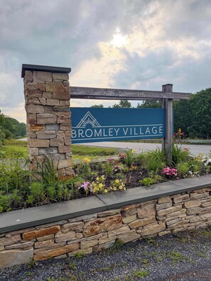 A sign for Bromley Village with a stone pillar and flower bed.