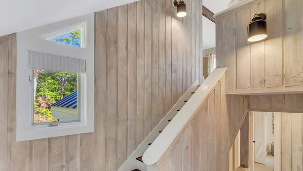 Un intérieur en bois avec un escalier, une fenêtre donnant sur un paysage verdoyant et une porte menant à une autre pièce.