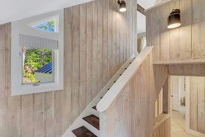 A wooden interior with a staircase, a window with a view of greenery, and a door leading to another room.