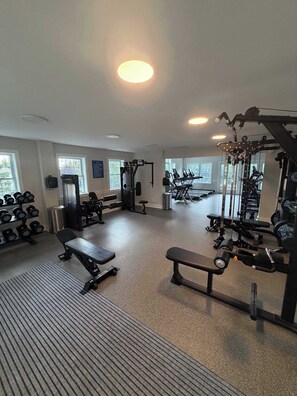 Ein Fitnessraum mit verschiedenen Trainingsgeräten, darunter Kurzhanteln, Bänke und Kraftgeräte.