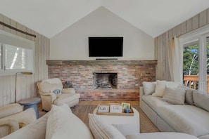 A living room with a brick fireplace, a flat-screen TV mounted above it, and two sofas.