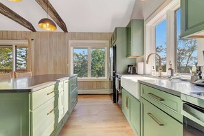 A modern kitchen with green cabinets, a large window, and wooden beams on the ceiling.