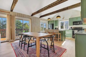 Een ruime keuken met houten balken, een eethoek met een grote tafel en stoelen, en uitzicht op de omgeving door grote ramen.