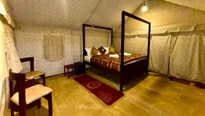 Una cama con dosel en una habitación con piso de piedra, una pequeña silla de madera y un tapete rojo estampado.