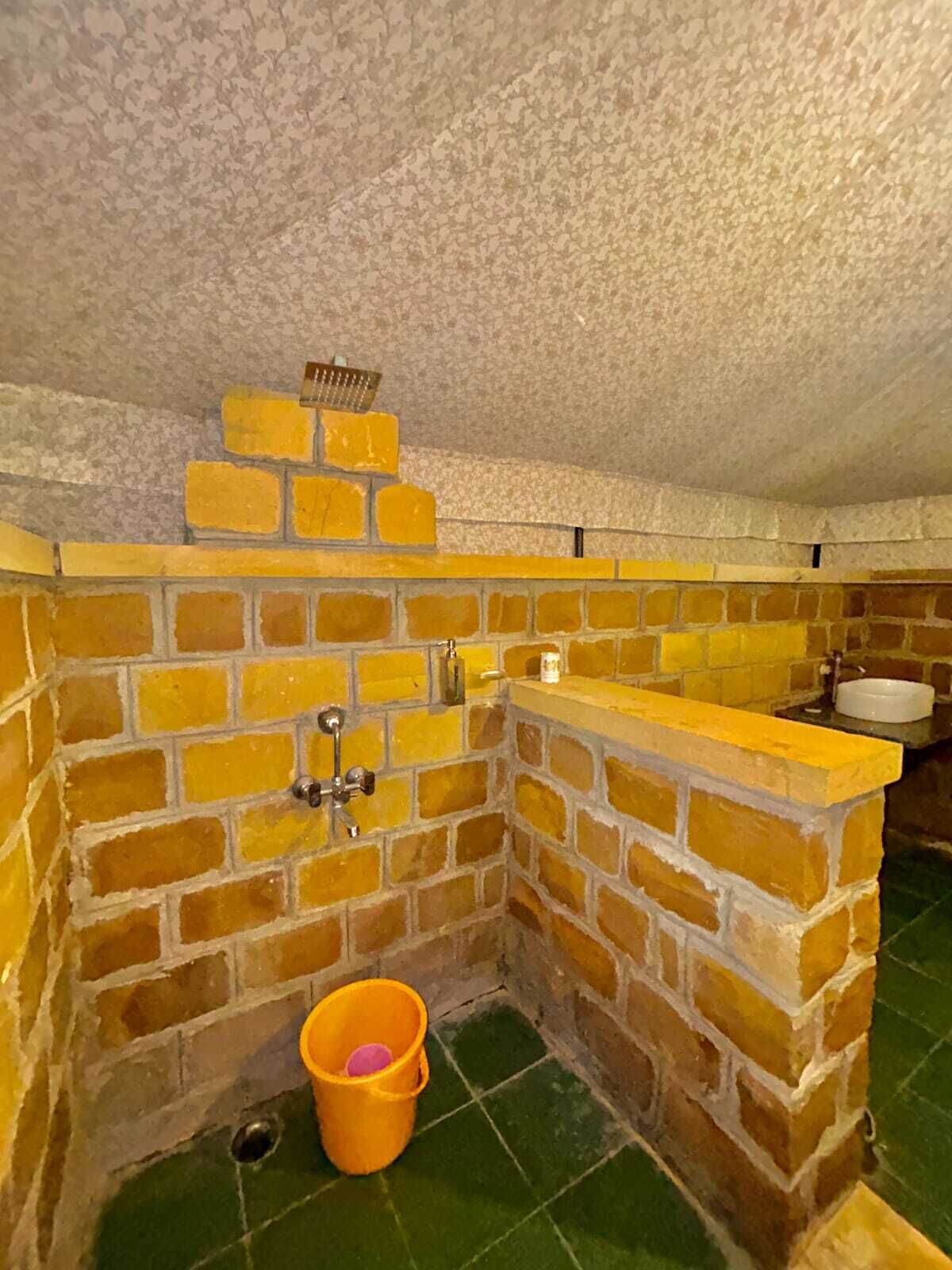 A small, enclosed bathroom with a brick wall, a yellow bucket, and a white sink.