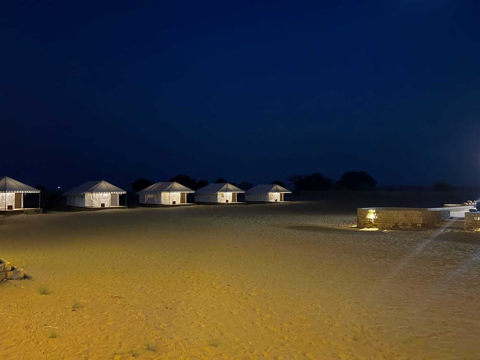 A row of white tents with a sandy ground, under a dark sky.
