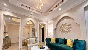 Een ruime woonkamer met een groene veloursbank, twee witte ronde salontafels en een kroonluchter.