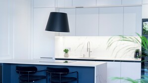 Een moderne keuken met een marmeren spatwand, een zwarte hanglamp en twee barkrukken.
