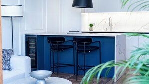 Een moderne keuken met een marmeren aanrecht, zwarte barkrukken en een zwarte hanglamp.