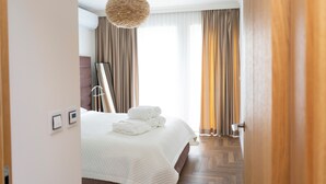 Een hotelkamer met een bed, een groot raam met gordijnen, een hanglamp en een houten vloer.