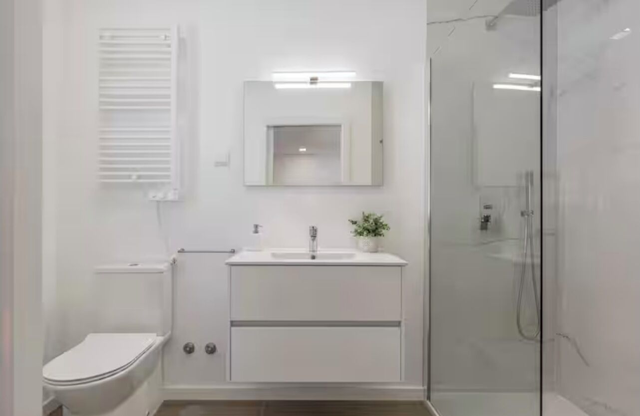 Un baño moderno con inodoro, lavabo, espejo y cabina de ducha de vidrio.