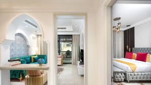 Habitación de hotel con cama, zona de estar con sofá y sillones, televisión y balcón con vistas.