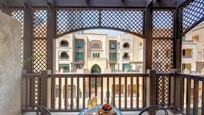 Un balcón con una mesa preparada para dos personas, un cuenco decorativo y vistas de un edificio con ventanas y balcones arqueados.