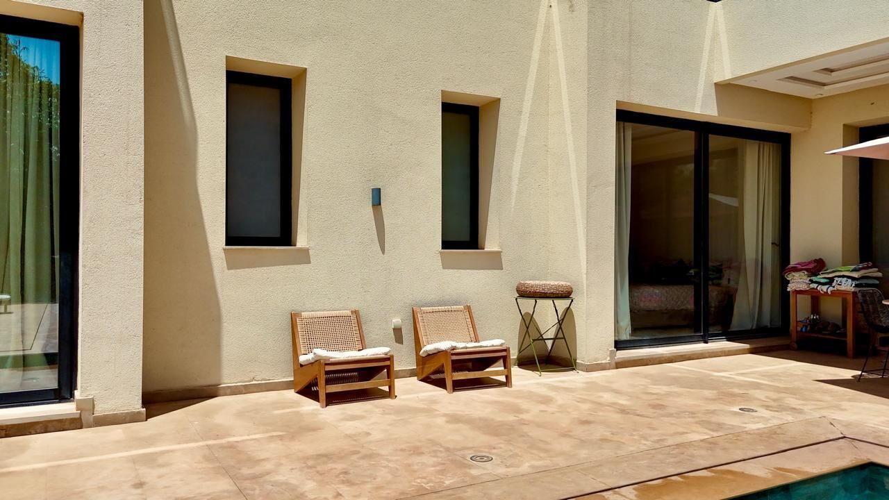 A poolside area with two wooden lounge chairs, a small table, and a chair.