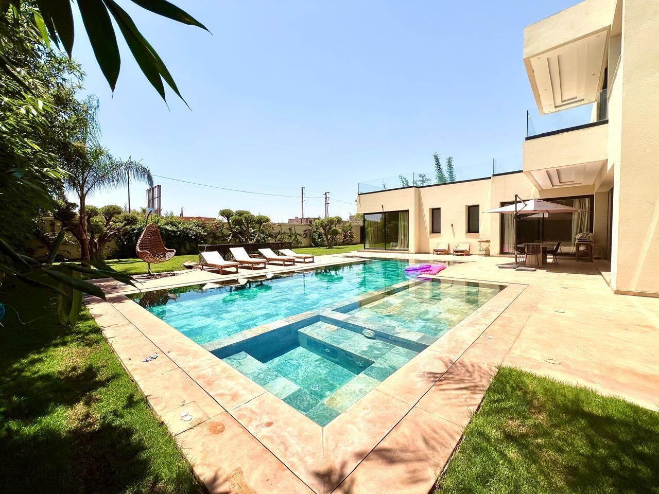 Une piscine rectangulaire, bordée d’une terrasse carrelée, entourée d’une pelouse et d’un bâtiment doté d’un toit plat.