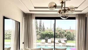A modern living room with a sectional sofa, a glass coffee table, and a view of a swimming pool. - VILLA KECH (Marrakech)