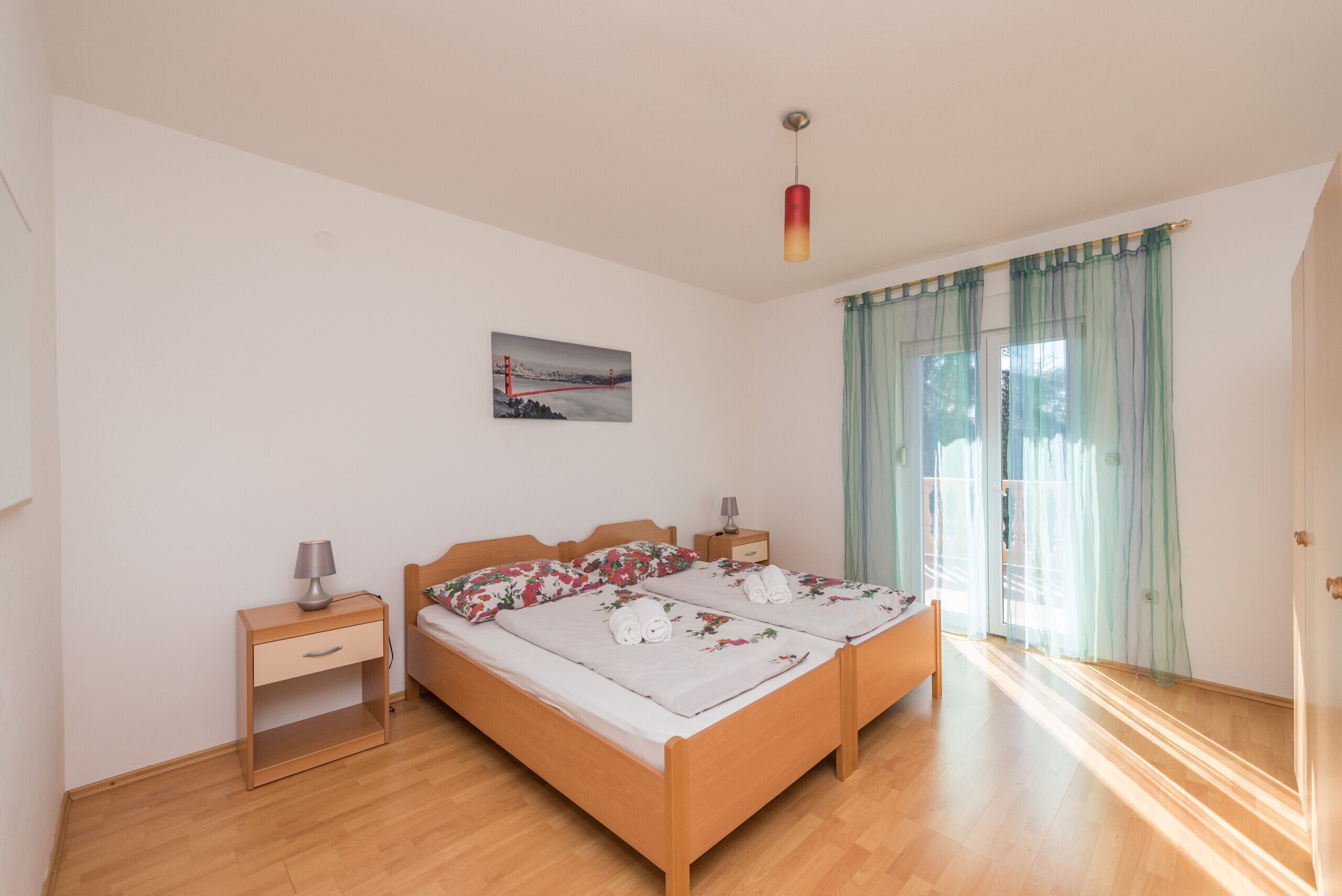 Ein Doppelbett mit floralem Bettzeug, ein Nachttisch mit Lampe und ein Bild an der Wand.
