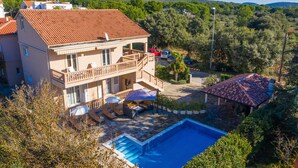 A two-story house with a swimming pool, a covered patio, and a view of the surrounding greenery.