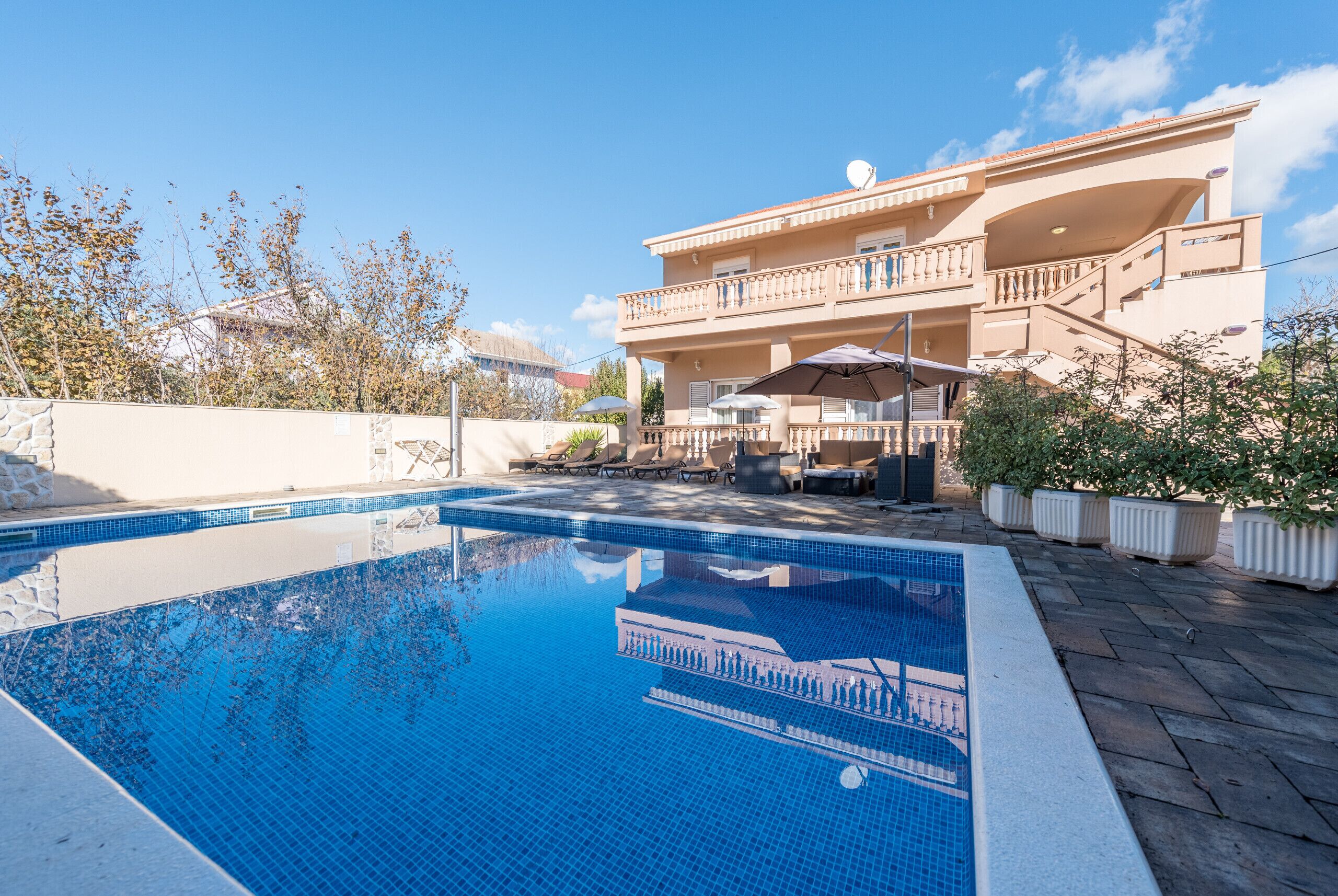 A swimming pool with a clear blue water surface, surrounded by a stone wall and potted plants.