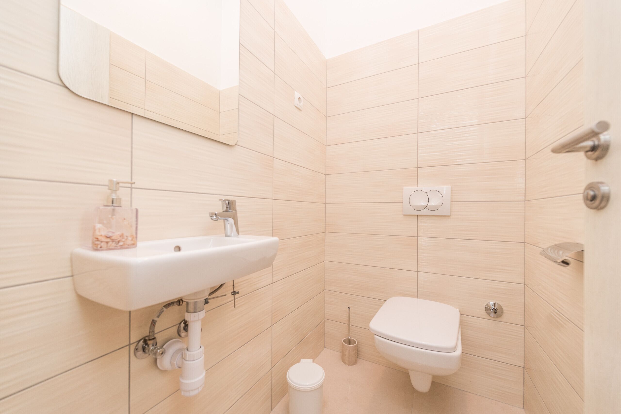 Un baño pequeño y moderno con lavamanos, inodoro y espejo blancos.