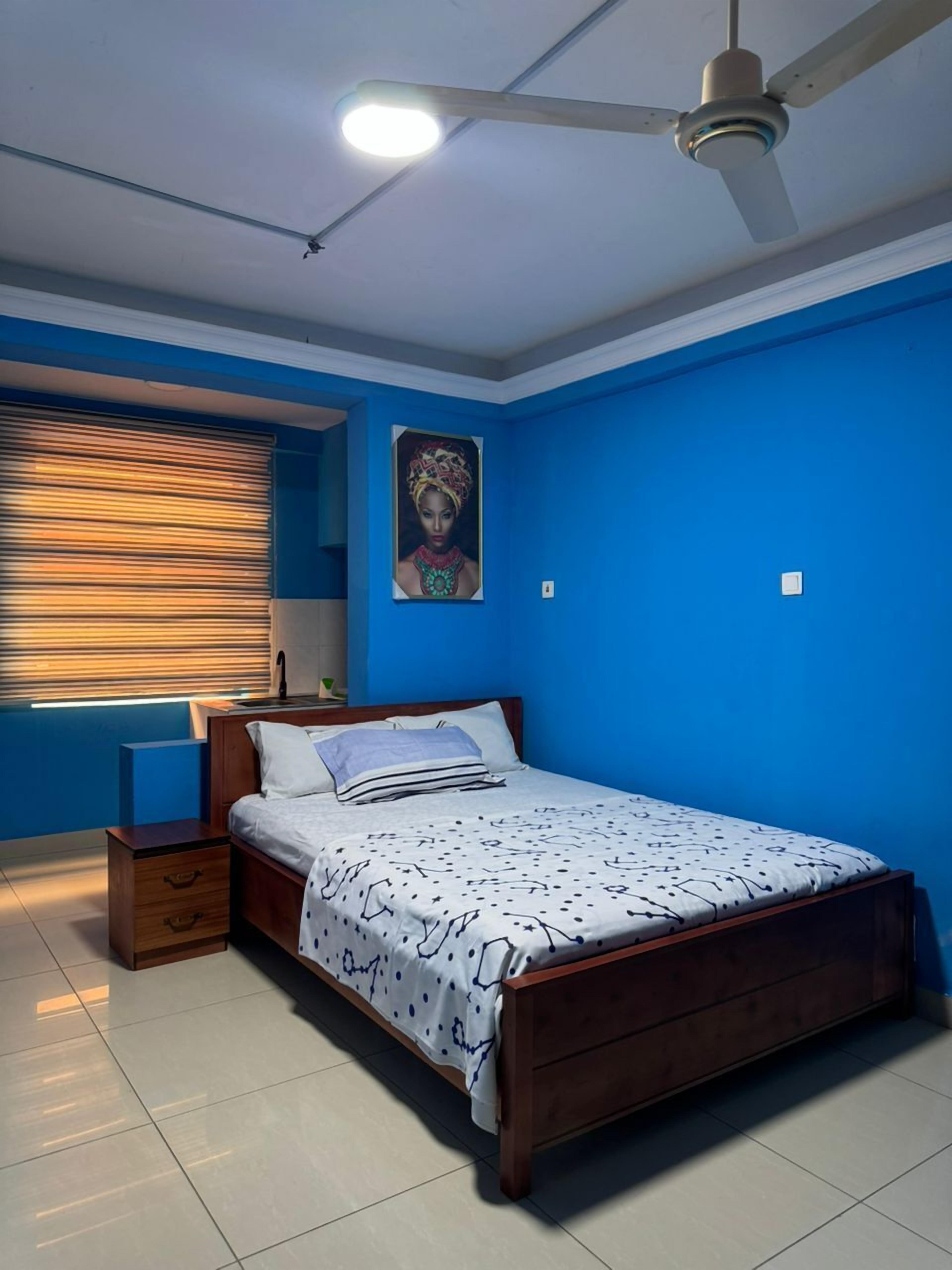 A bedroom with a bed, a nightstand, a ceiling fan, a window with blinds, and a painting on the wall.