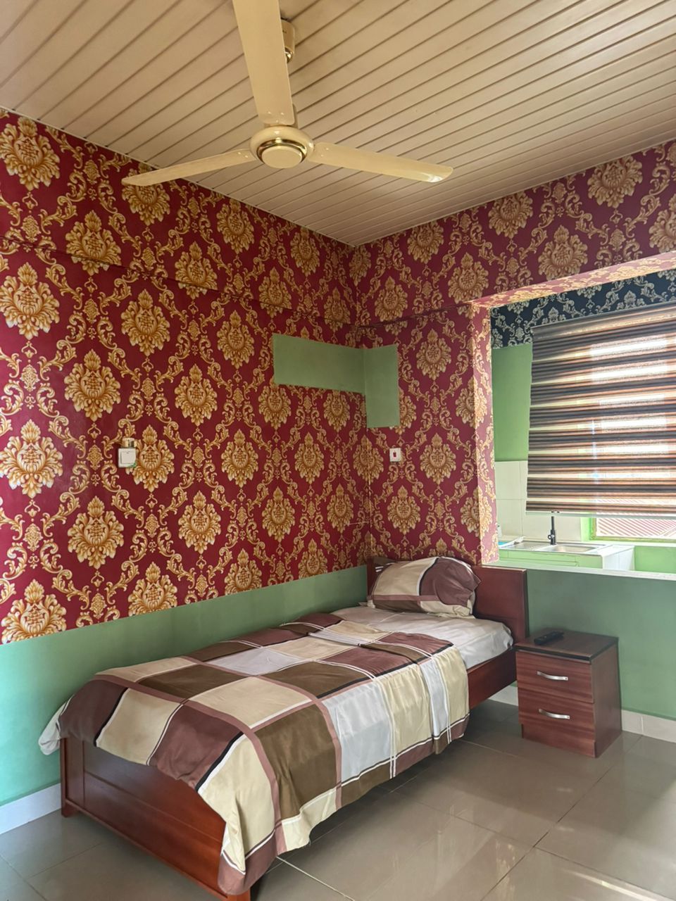 A bedroom with a bed, a nightstand, a green headboard, a ceiling fan, and a window with blinds.