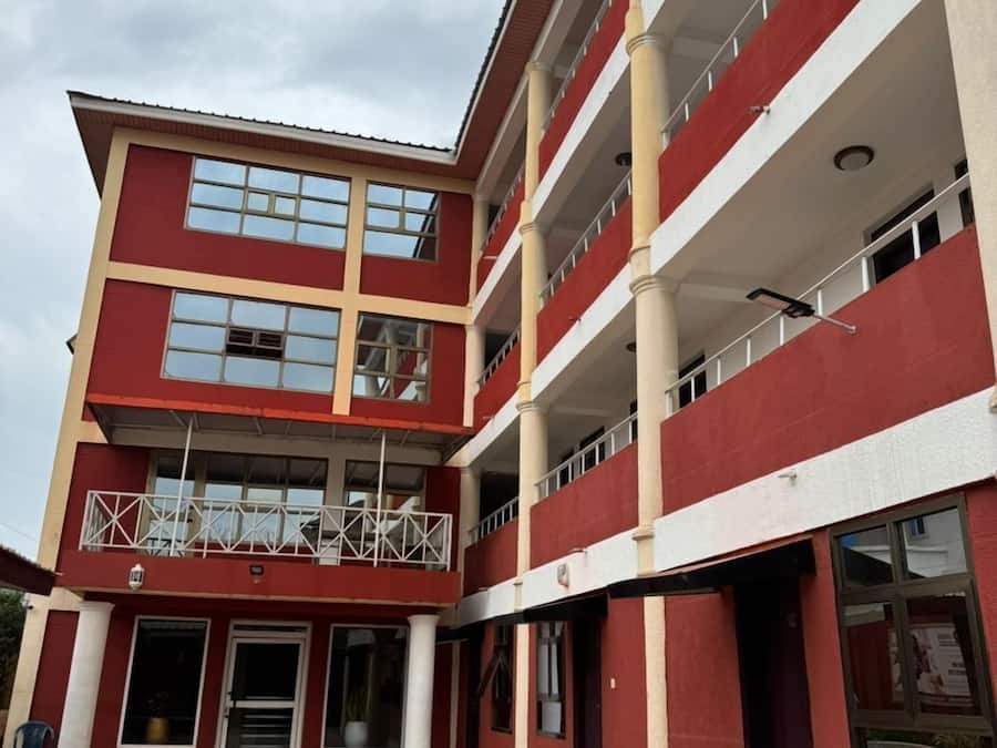 Un edificio de varios pisos con fachada roja y blanca, múltiples balcones y un patio empedrado.