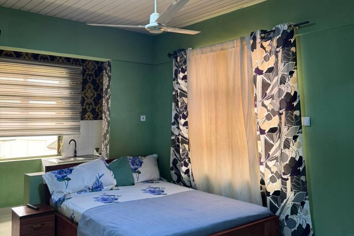 A bedroom with a bed, a nightstand, a ceiling fan, and a window with blinds.