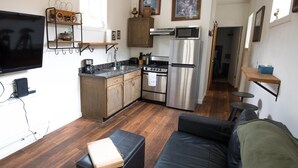 A compact kitchen with modern appliances, a flat-screen TV, and a dining area with a sofa and ottoman.