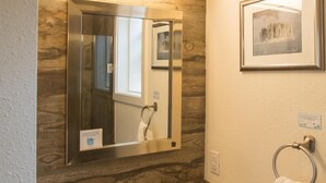 A bathroom with a wooden vanity, a glass sink, a mirror, a towel ring, and a framed picture on the wall.