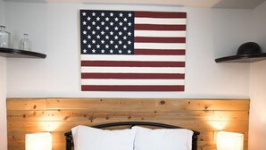 Une chambre à coucher avec une tête de lit en bois, un lit avec des oreillers blancs, deux lampes de chevet et un drapeau américain accroché au mur.