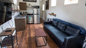 Un espace de vie compact comprenant un coin cuisine, un canapé en cuir noir, une table basse en bois et une table à manger.