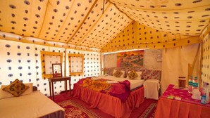 A tented room with a bed, a table with water bottles, and a painting on the wall. - Royal Gadhvi Desert Camp (Jaisalmer)